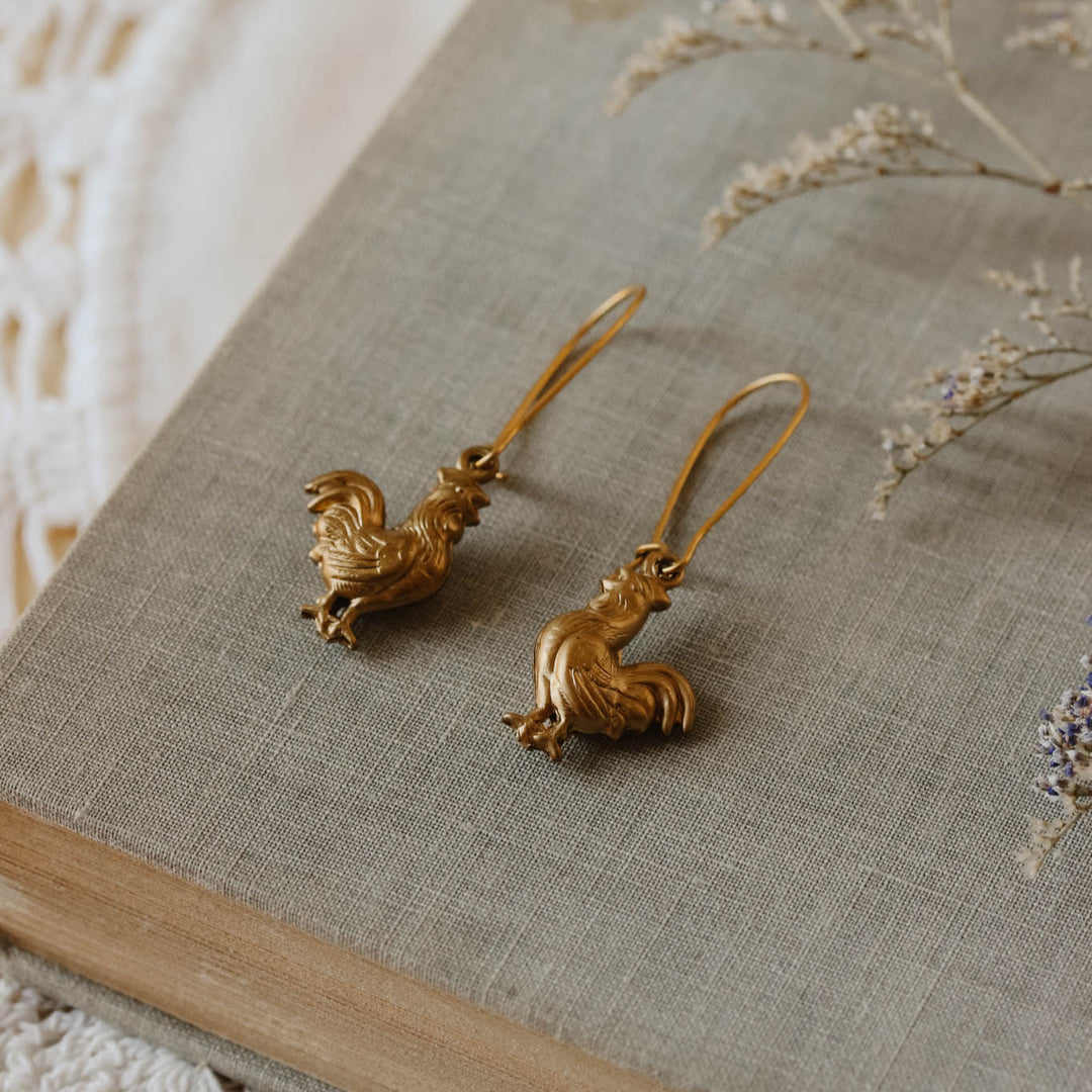 Gold earrings on a textured surface with dried flowers