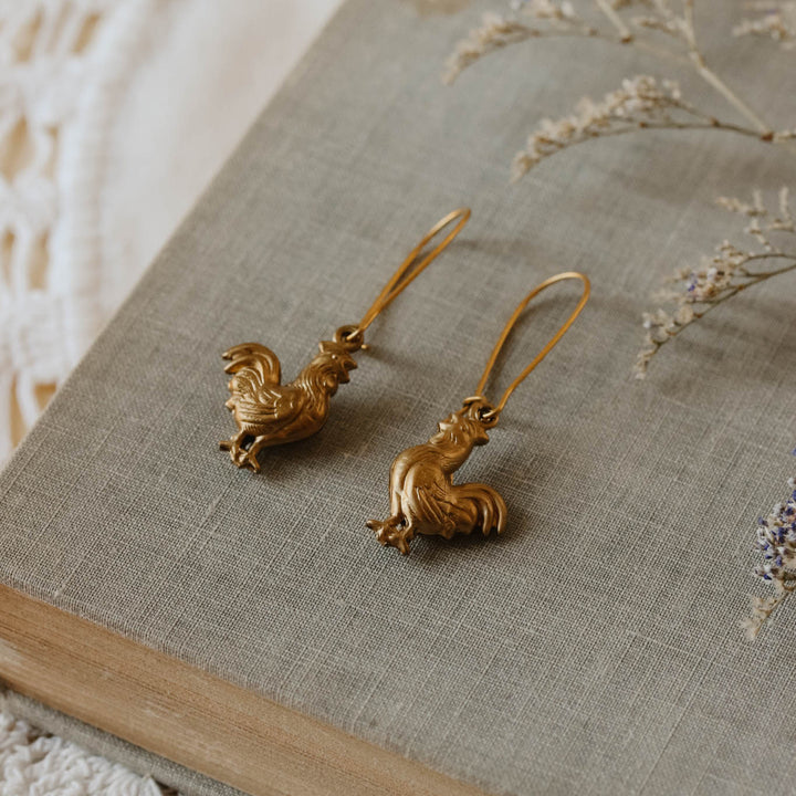 Gold earrings on a textured surface with dried flowers