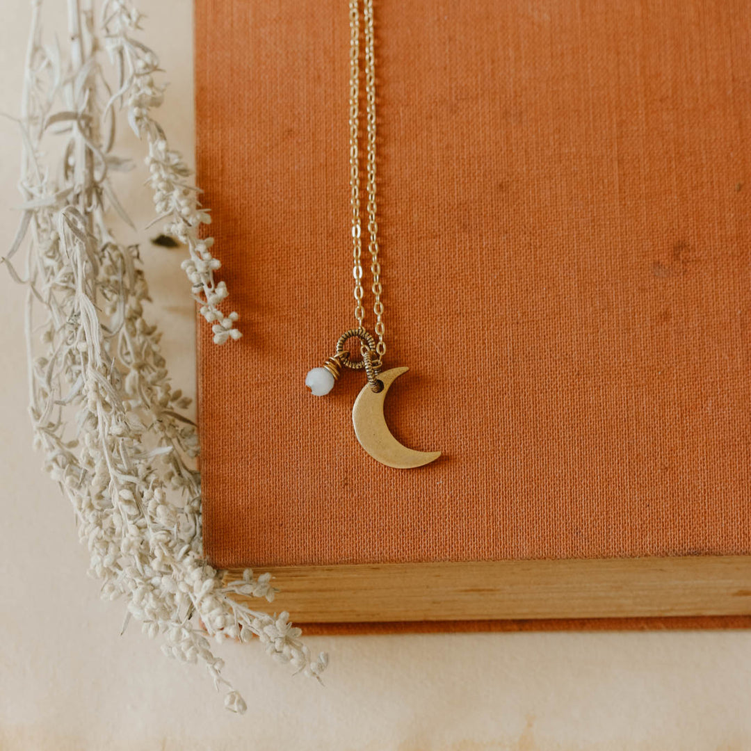 Necklace with a moon and pearl pendant on an orange fabric background