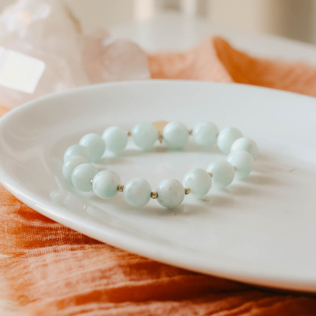 Light blue beaded bracelet on a white plate with an orange cloth background