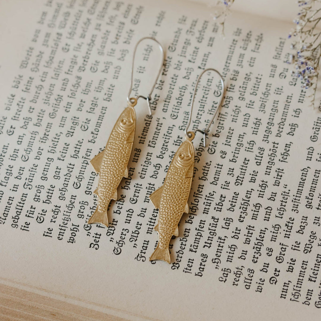 Gold fish-shaped earrings on an open book
