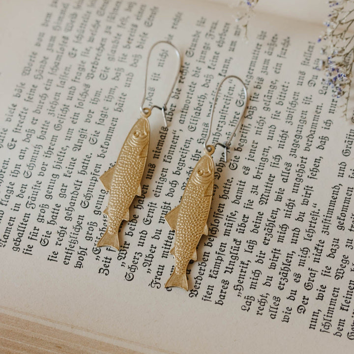 Gold fish-shaped earrings on an open book