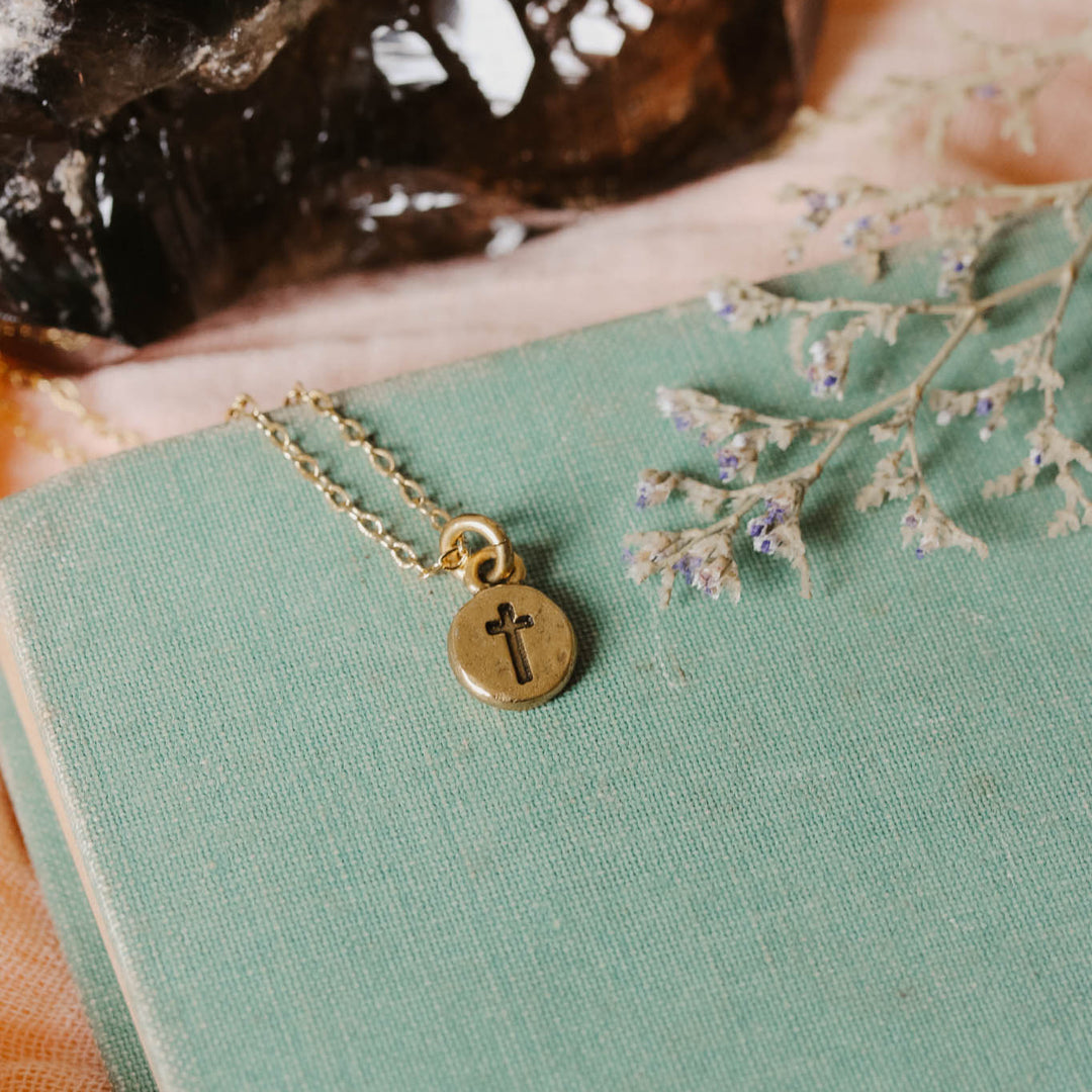 Gold necklace with a cross pendant on a green book with dried flowers