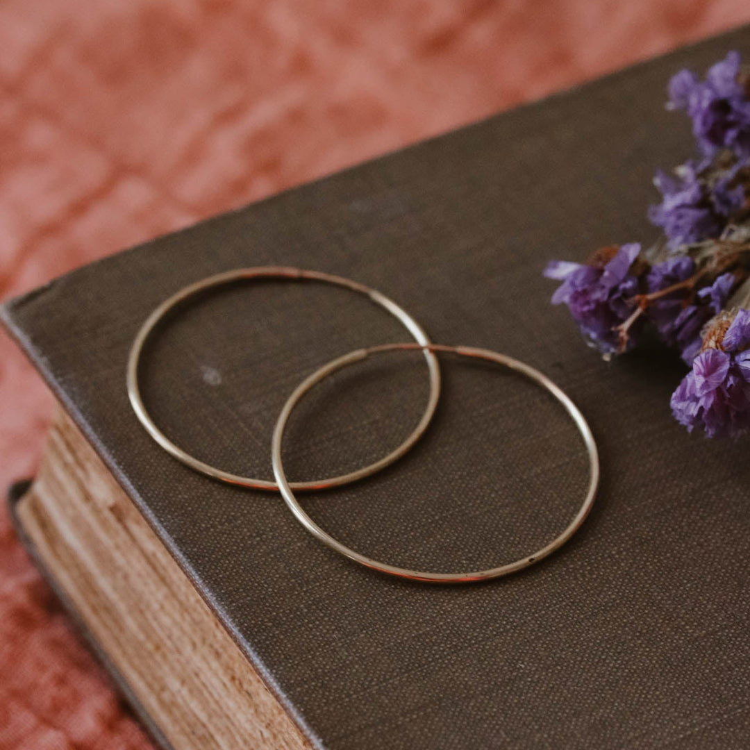 Gold hoop earrings on an old book with purple flowers