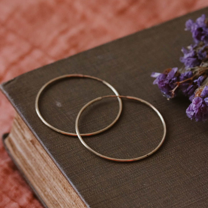 Gold hoop earrings on an old book with purple flowers