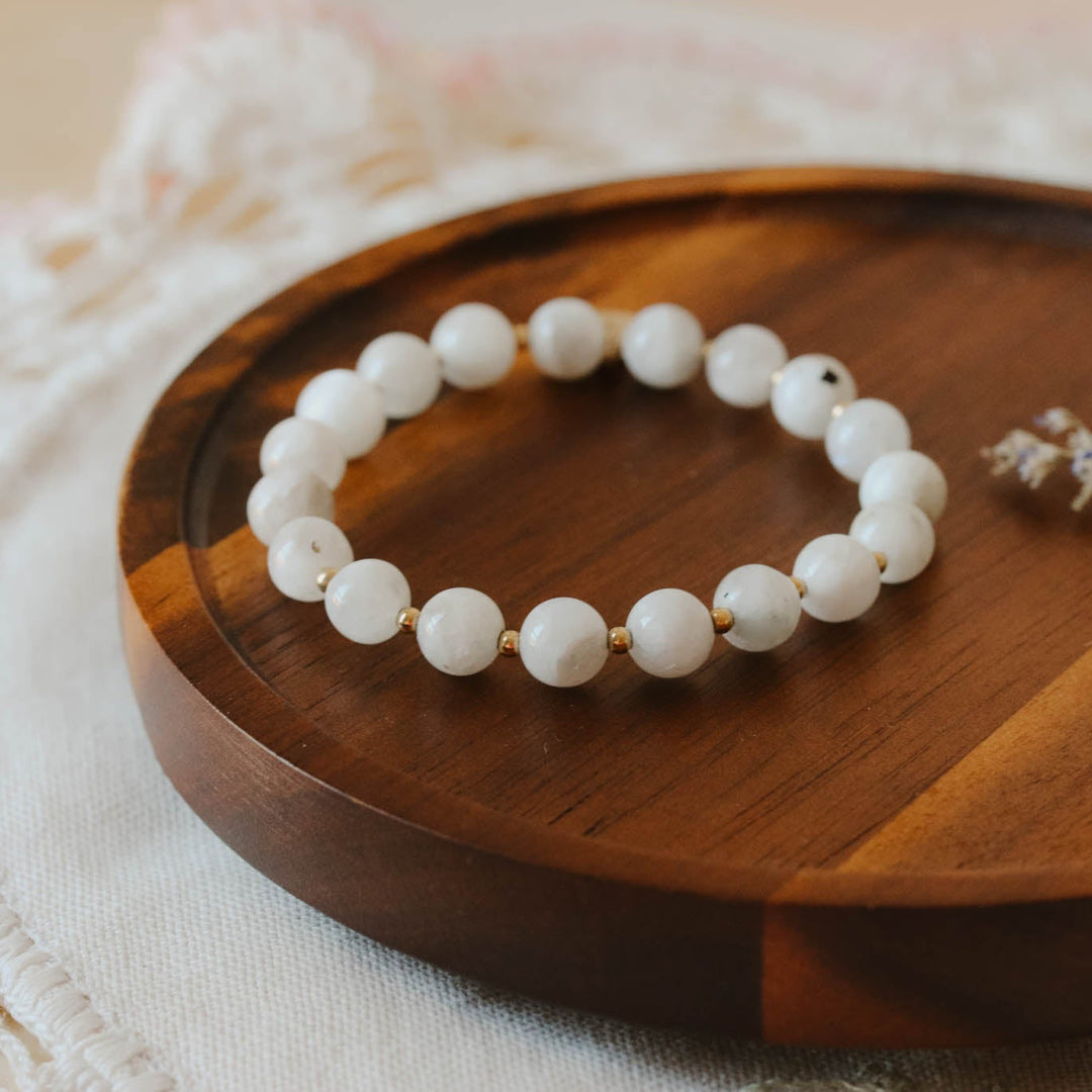 White beaded bracelet on a wooden plate with a delicate flower arrangement