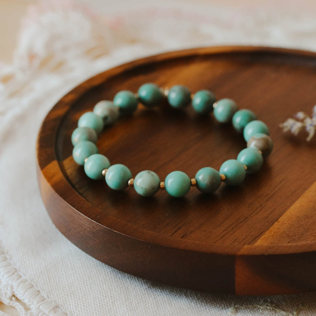 Turquoise beaded bracelet on a wooden plate with a delicate flower arrangement.