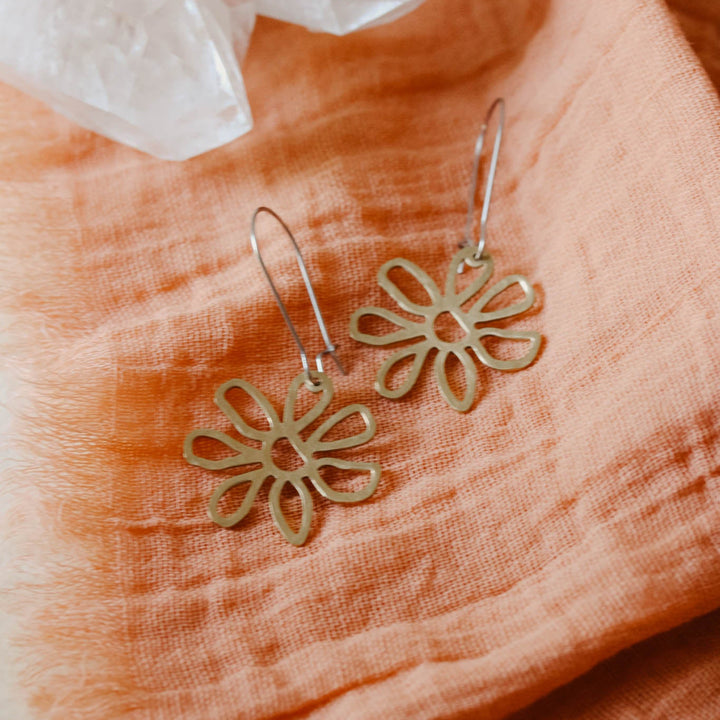 Gold flower-shaped earrings on a soft peach fabric background