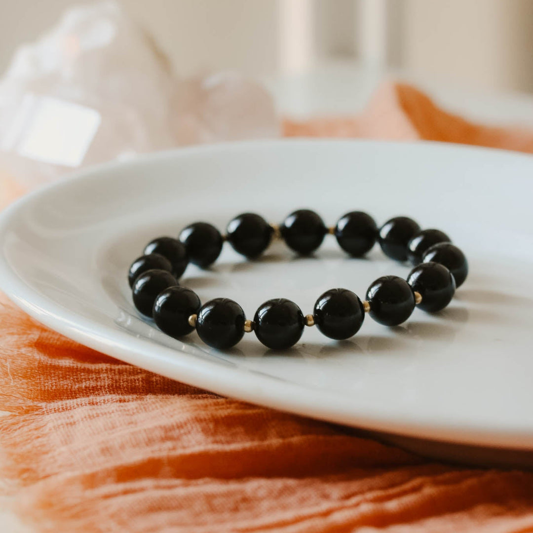 Black beaded bracelet on a white plate with an orange fabric background
