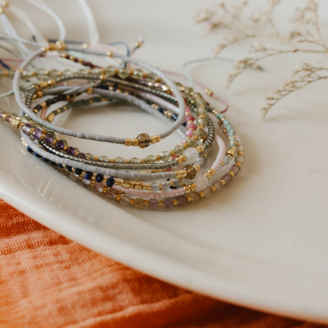 Stack of bracelets on a white dish with an orange fabric background