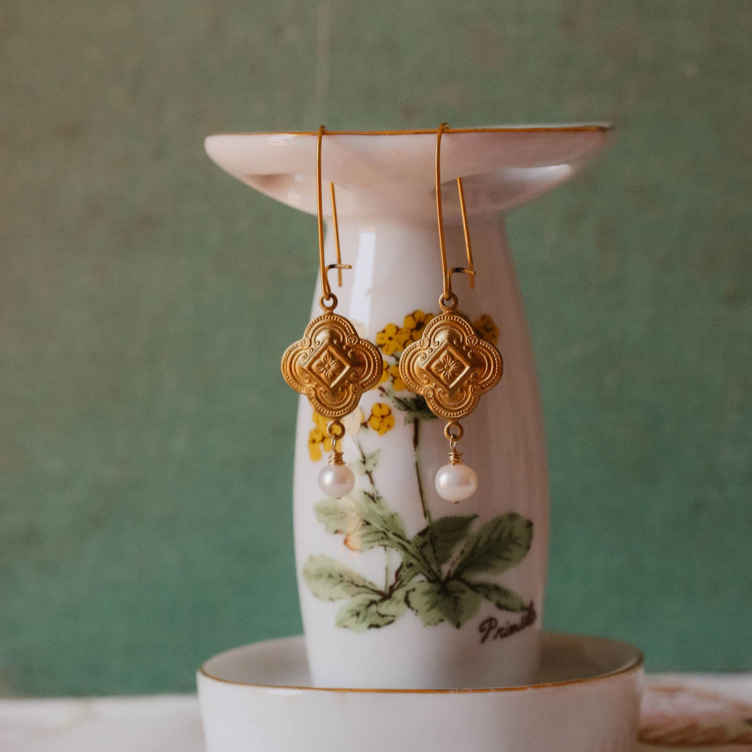 Gold earrings on a floral earring stand with a green background