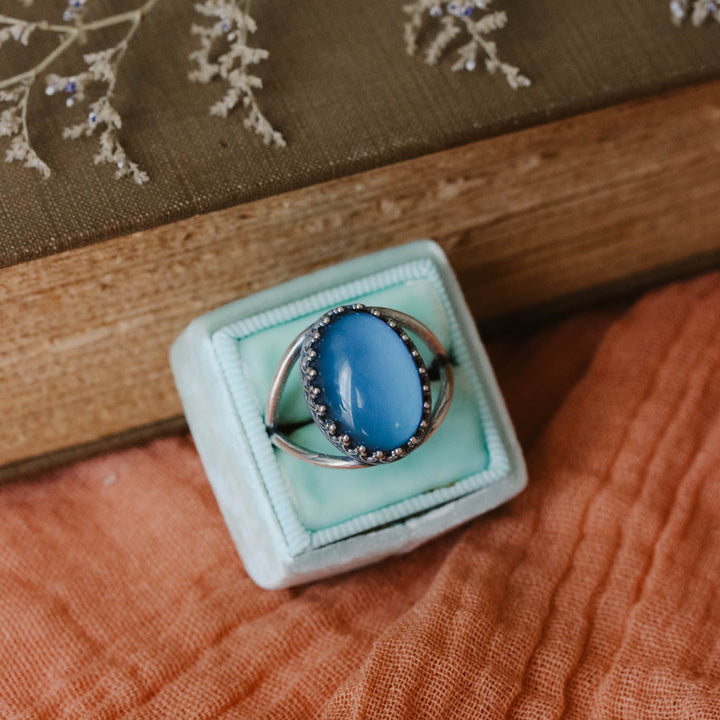 Blue ring in a green box on a wooden surface with floral embroidery