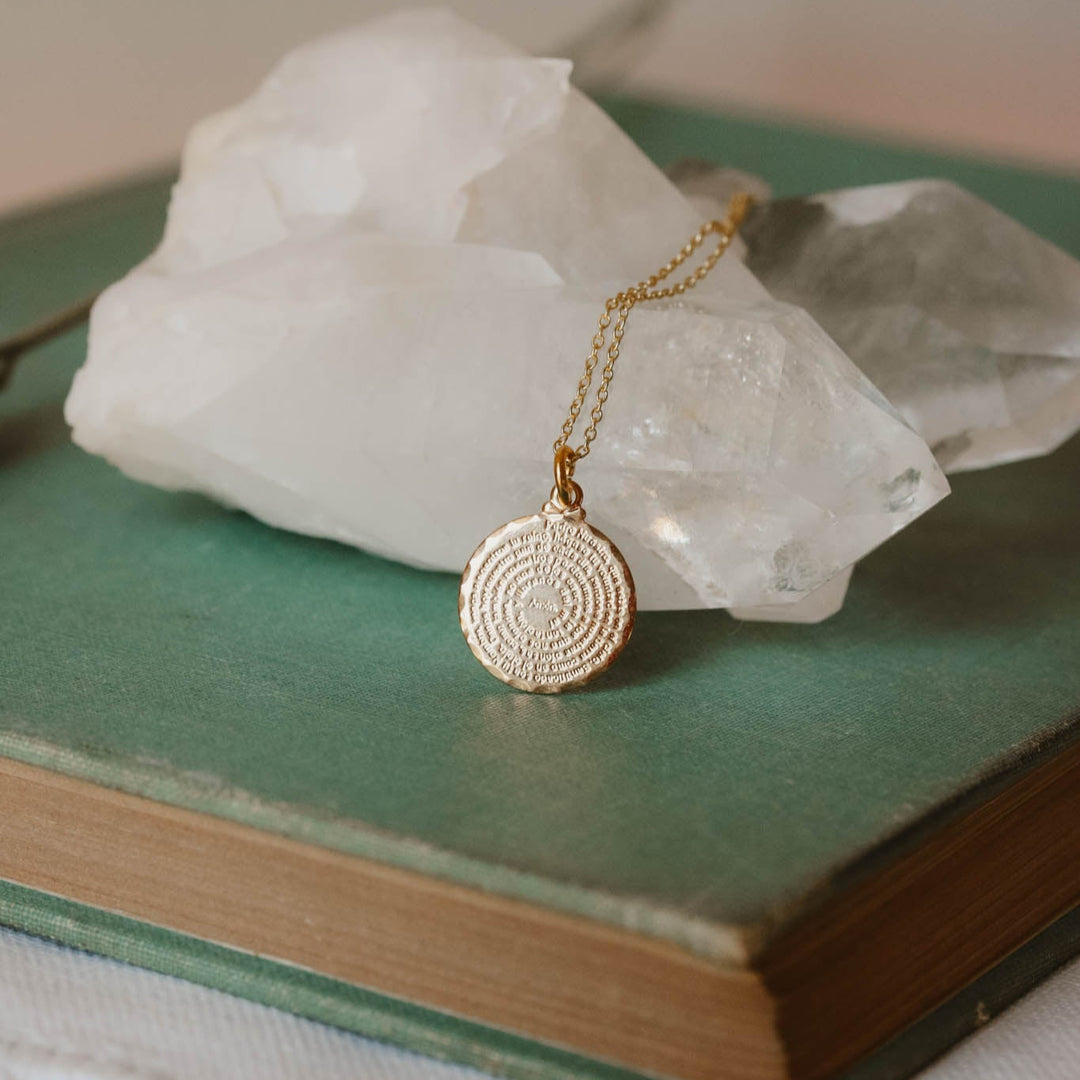 Gold necklace with a circular pendant on a book with crystal rocks in the background