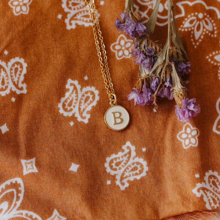 Necklace with a 'B' pendant on an orange fabric with white patterns
